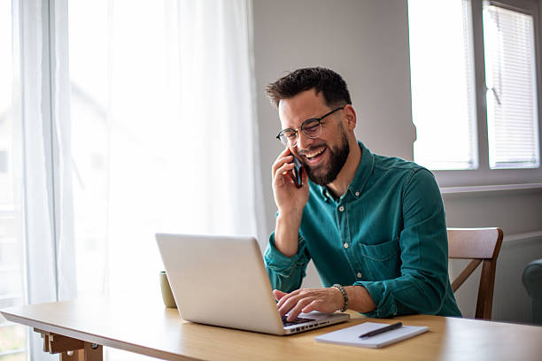istock Happy young man working from home, talking on the phone and using laptop 2217324589