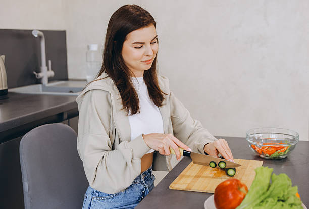 istock Young Woman Cutting Cucumber While Preparing Healthy Meal in Modern Kitchen 2217327764