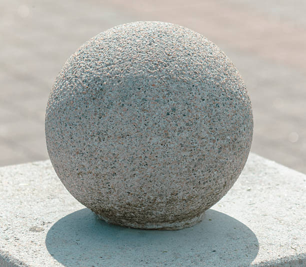 A large grey stone ball sits on a cement slab. The stone is smooth and round, with a slightly rough texture. The stone is placed on a grey surface, which gives the impression of a calm