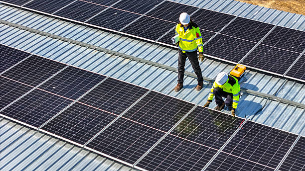 istock Two engineers in safety gear standing on a rooftop reviewing blueprints for a solar panel installation project, showcasing teamwork, renewable energy planning, and sustainable construction practices. 2217336530