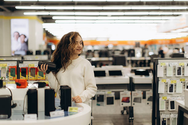 A smiling woman is holding a tablet device while engaging with appliances in a retail environment, reflecting a positive shopping experience in a modern store.