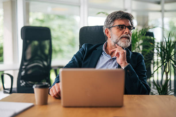 istock Senior businessman working on laptop in modern office, looking away thoughtfully 2217338564