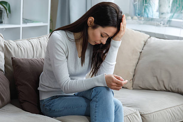 istock Young woman suffering from headache sitting on couch at home 2217342275