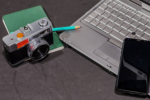 Workspace featuring a vintage camera resting on a notebook, alongside a laptop and smartphone for a blend of classic and modern technology.