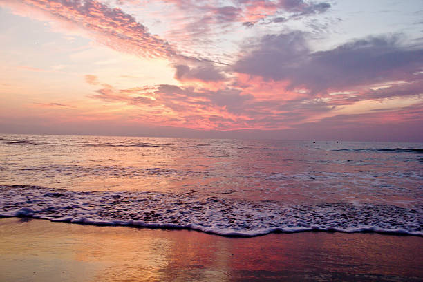 Close-to-ground perspective capturing foamy sea currents gently advancing on a Jalisco beach during a vivid sunset. The sky explodes in dramatic hues of orange, purple, and pink, mirrored by the water’s surface in a mesmerizing kaleidoscope of colors and shapes. This image stands out from traditional beach sunsets by emphasizing the texture and movement of the water combined with the fiery sky. Ideal for travel blogs, environmental campaigns, coastal tourism marketing, or art prints seeking dynamic and atmospheric seascapes.
