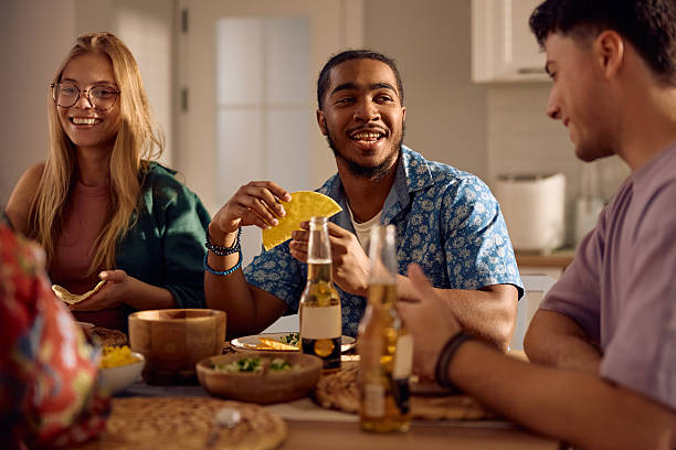 istock Happy black man eating tacos while talking to his friends at dining table. 2217347939