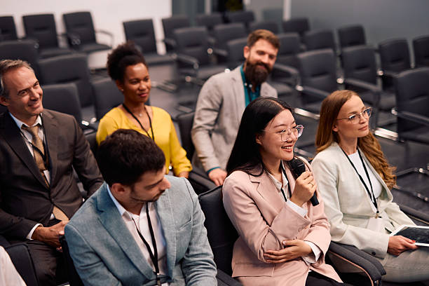 istock Young businesswoman speaking at a conference using a microphone, sitting in the audience 2217360215