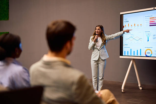 istock Businesswoman using microphone pointing at graph on projection screen during a presentation 2217360437