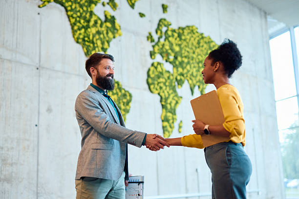 istock Business partners shaking hands in a modern office with a green world map 2217360743