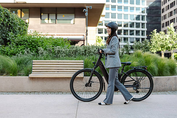 Confident business professional riding a bike while wearing a suit and helmet in a modern city downtown area, promoting eco-friendly transportation, health benefits, and a balanced work lifestyle.