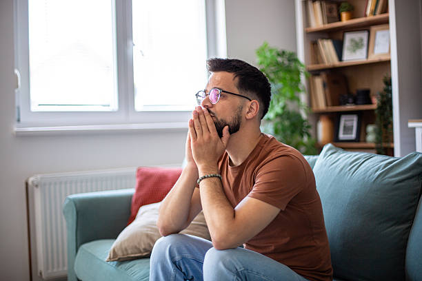 istock Depressed young man sitting on sofa covering his mouth with his hands 2217365033
