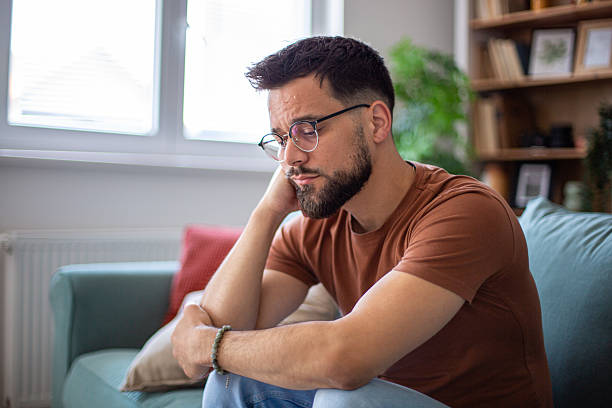 istock Sad young man sitting on sofa at home feeling depressed 2217365134