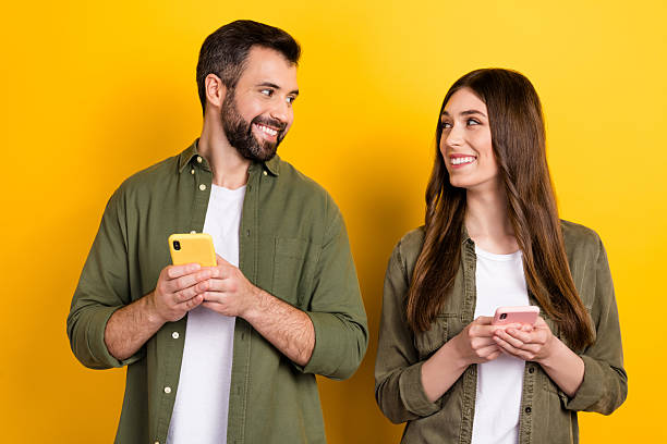 istock Portrait of attractive cheerful couple using device chatting app 5g post smm isolated over bright yellow color background 2217367495