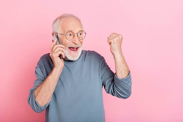 istock Photo of excited lucky retired man grey sweater spectacles looking empty space talking gadget isolated pink color background 2217367902