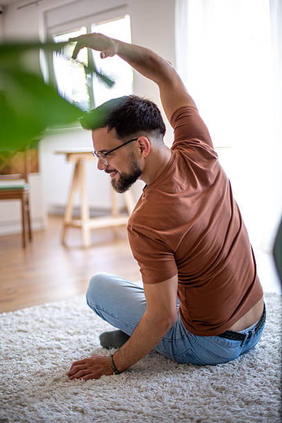 istock Young man stretching his back while sitting on the floor at home 2217369275