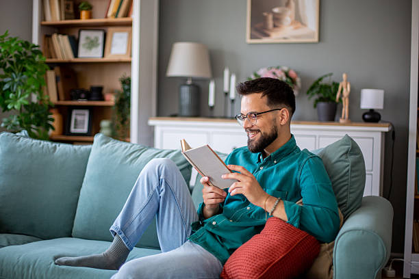 istock Young man relaxing on sofa reading a book at home 2217369408