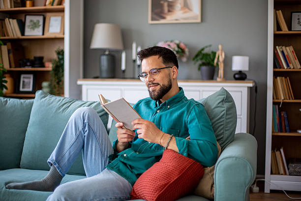 istock Young man relaxing on sofa reading a book at home 2217369409