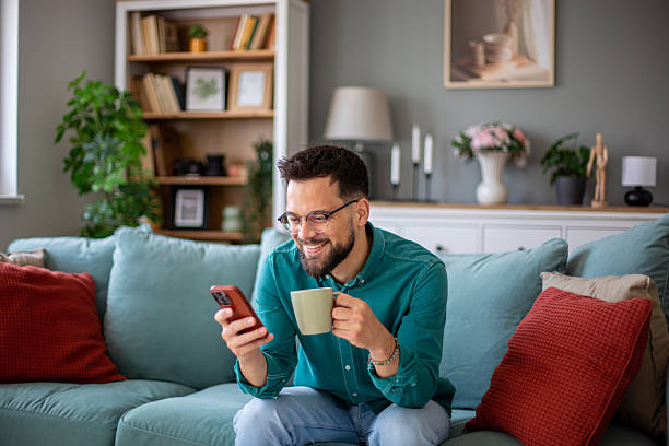istock Young man relaxing on sofa, enjoying coffee and browsing smartphone at home 2217369672