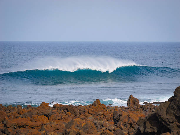 istock Large wave with an arc of offshore mist breaking beyond rugged volcanic coast 2217369965