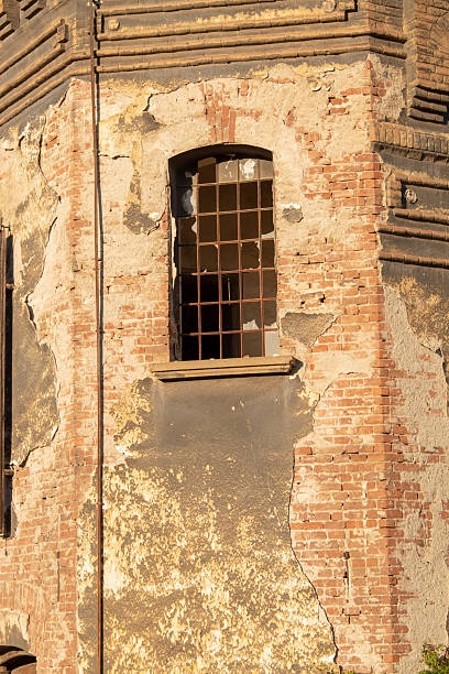 istock Old damaged wall with peeling plaster, red bricks detail and window, a rustic urban decay background 2217372438