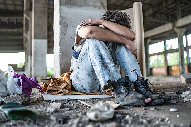 A person sits in a neglected urban space, reflecting themes of hardship, isolation, and life challenges.