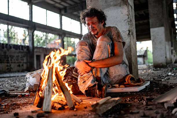 istock Man Sitting by Fire in an Abandoned Building During Sunset 2217377065