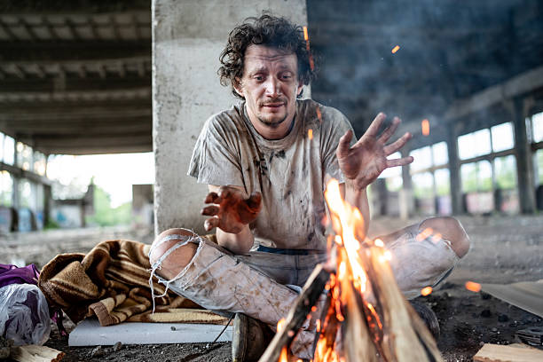 Man Warming Hands by Fire in Abandoned Building Wearing Worn Clothing