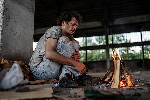 istock Man Seeking Warmth by Campfire in an Abandoned Industrial Setting 2217377084