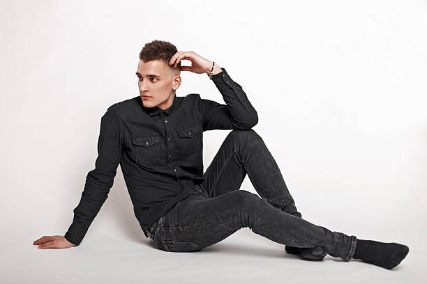 istock Handsome young man in black clothes sitting on a white background 2217379678