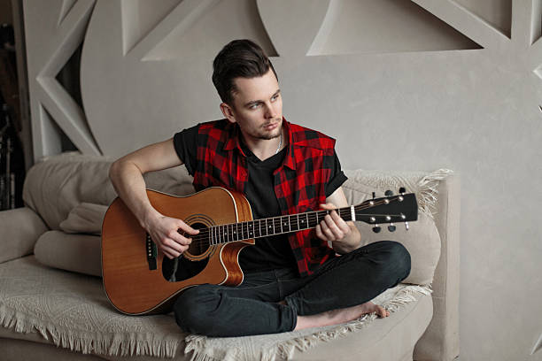 istock Young handsome man sitting on sofa and playing guitar 2217379743