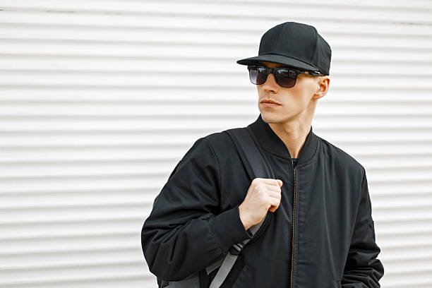istock Handsome young man with sunglasses in a black baseball cap and jacket with a bag 2217379923