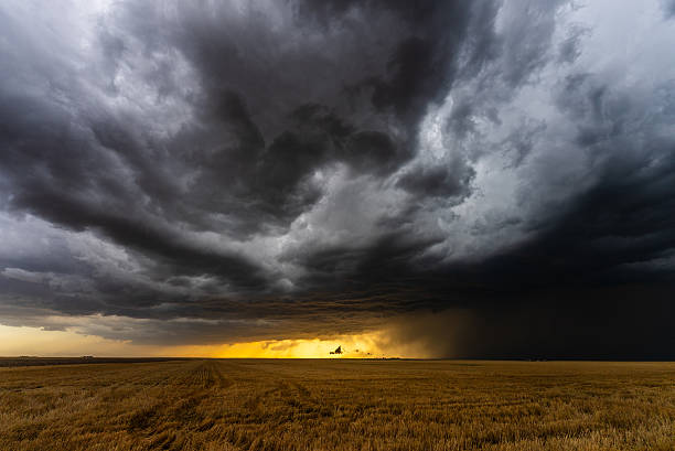 Warm sun set light below dark storm clouds moving across over fields
