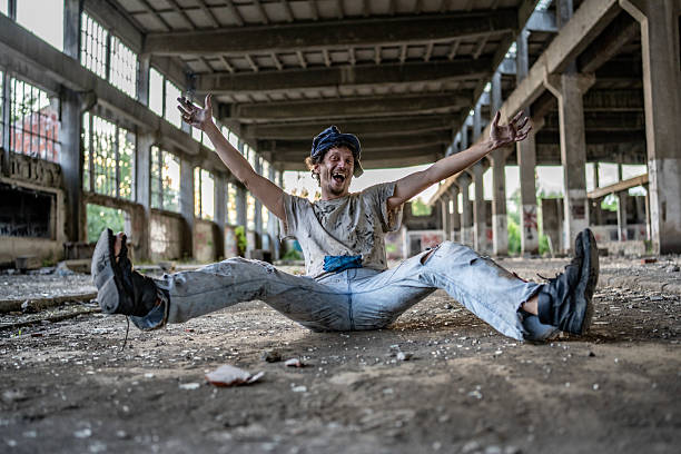 An energetic man in casual attire poses cheerfully inside a vast, deserted industrial warehouse, exuding positivity and high spirits. The backdrop accentuates the rustic and vibrant mood of the scene.