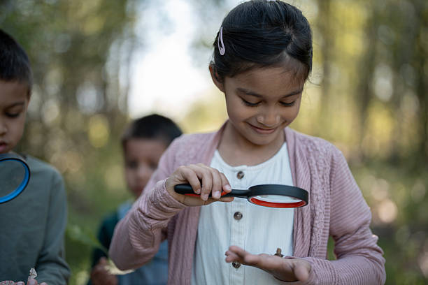 Young children examine the outdoors using magnifying glasses, fostering curiosity and learning about nature. The scene emphasizes exploration, education, and a connection with the natural world in a group setting.