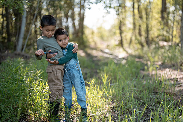 Two young boys stand together in a sunlit forest, sharing a moment of friendship and curiosity surrounded by lush greenery, symbolizing the wonder of nature and childhood exploration.