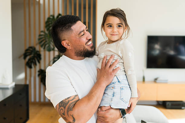 Affectionate Maori father with his cute little daughter, gazing at her daughter with love and having a big smile on his face.