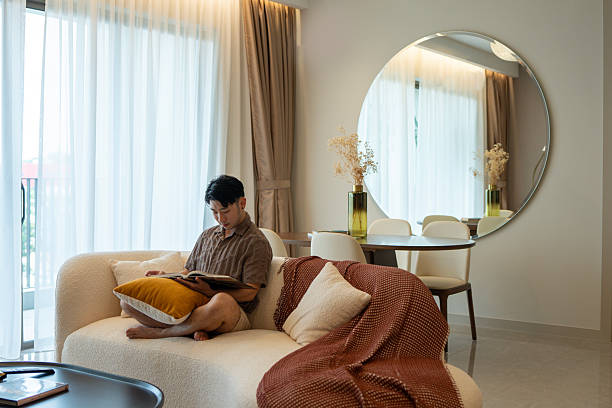 istock Young Asian Man Reading on Sofa in Bright, Modern Living Room 2217393208