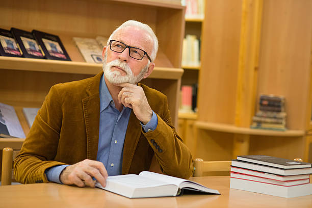 Senior man with gray hair and gray beard reading books in the library