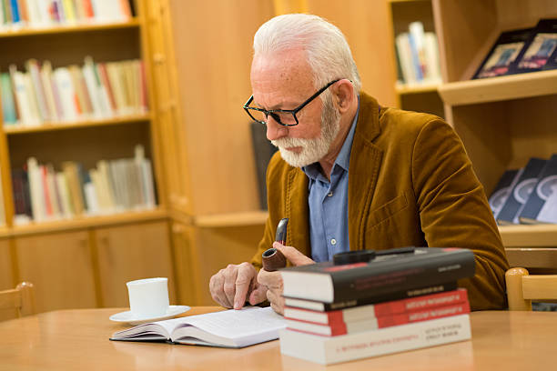 istock Senior man reading books in the library 2217395874