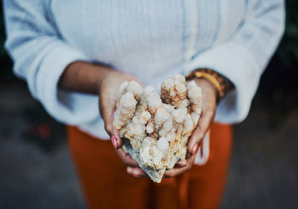 A close-up of feminine hands holding a sparkling quartz crystal cluster with earthy tones.