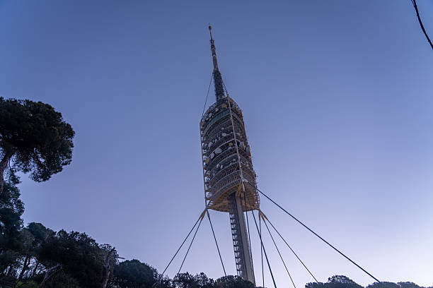 The Torre de Collserola, a telecommunications tower in Barcelona, Spain, stands tall against a clear blue sky, its unique design and purpose evident in its structure and surroundings.