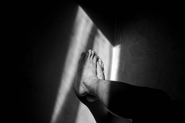 istock Human Legs Resting Against Wall in Monochrome Dramatic Light 2217399789