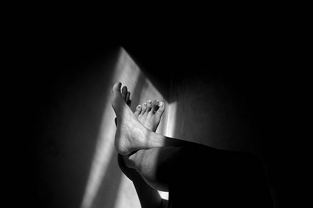 istock Human Legs Resting Against Wall in Monochrome Dramatic Light 2217399808