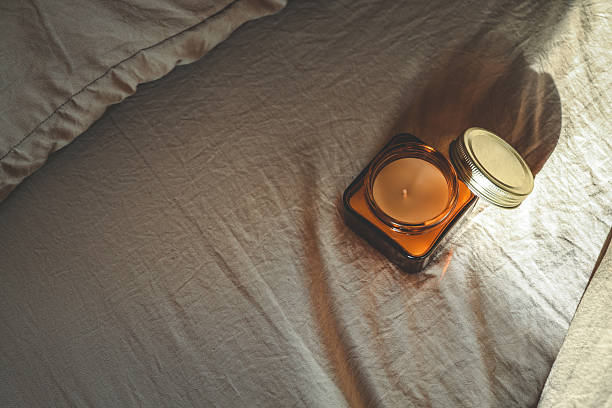 istock Amber glass candle with open lid placed on soft beige bedding in warm natural light, creating a minimalist and cozy composition ideal for peaceful mornings 2217401190