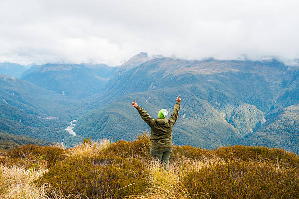 Solo hiker out in nature at weekend raising arms being successful while looking at the majestic mountain scenery Routeburn Track, South Island, New Zealand.