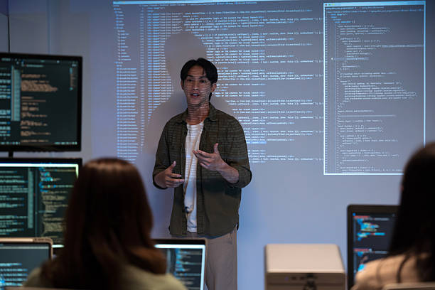 Asian man presents code using a projector during a software development meeting or coding workshop, guiding attendees through problem-solving and programming concepts in an educational setting. stock photo