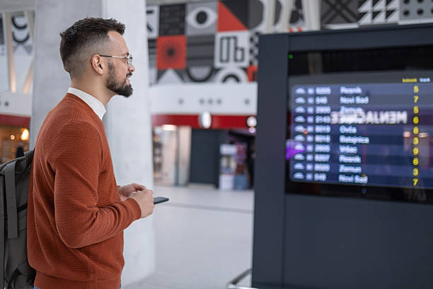 istock Airport Terminal: Young Man Looking at Arrival and Departure Information Display Looking for His Flight 2217415901