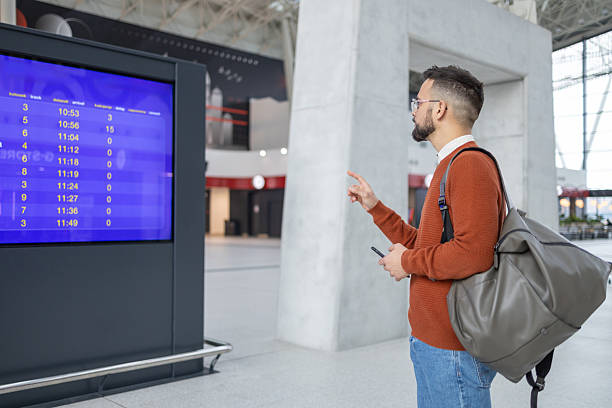 istock Airport Terminal: Young Man Looking at Arrival and Departure Information Display Looking for His Flight 2217415906