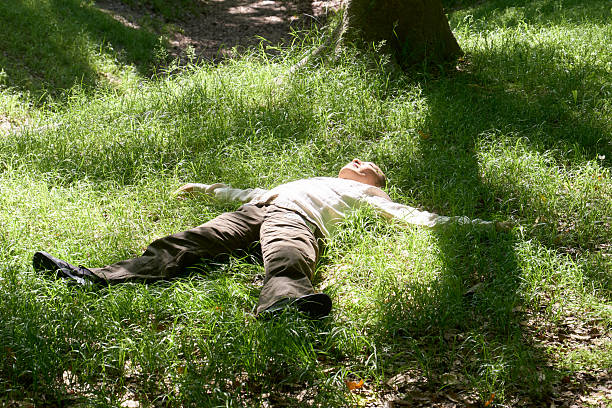 A man relaxes lying on the grass with the sun shining through the trees