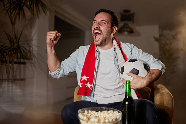 Cheerful man having fun while celebrating the goal of his favorite soccer team on TV at home.